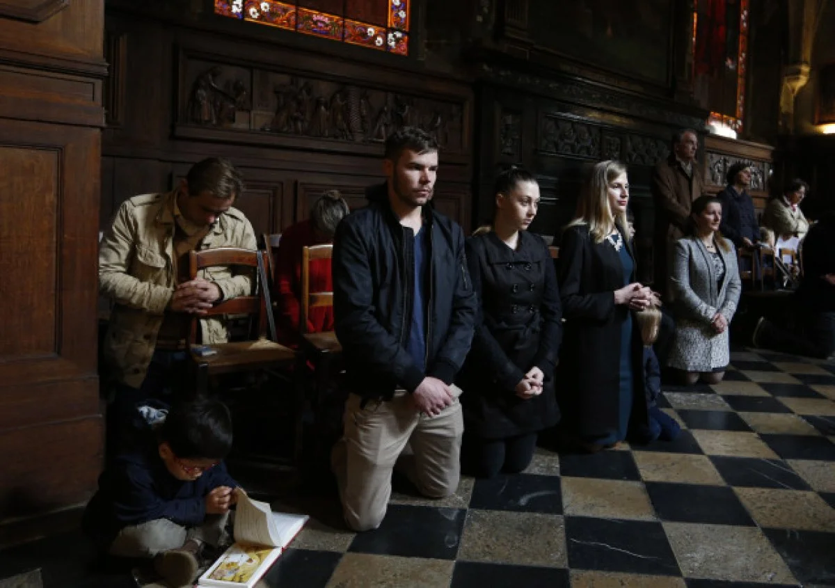People kneel during a Paris Mass for the 129 victims of coordinated terrorists attacks