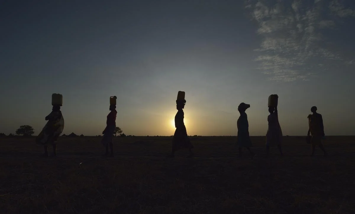 Women carry water to their homes at sunrise in Dong Boma, a Dinka village in South Sudan's Jonglei State. The women obtained water from a well drilled by the Lutheran World Federation, a member of the ACT Alliance, which is helping villagers restart their lives with support for housing, livelihood, and food security