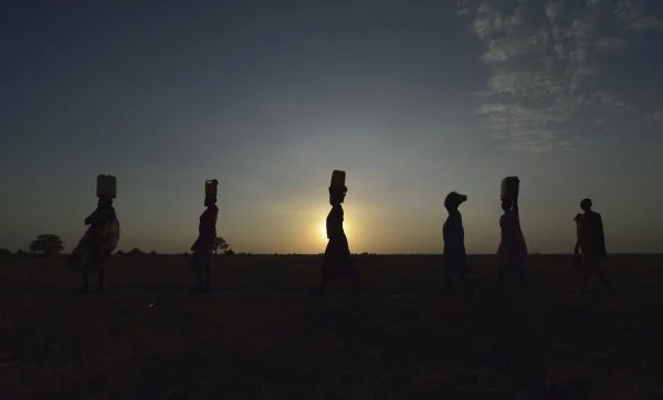   Women carry water to their homes at sunrise in Dong Boma, a Dinka village in South Sudan's Jonglei State. The women obtained water from a well drilled by the Lutheran World Federation, a member of the ACT Alliance, which is helping villagers restart their lives with support for housing, livelihood, and food security