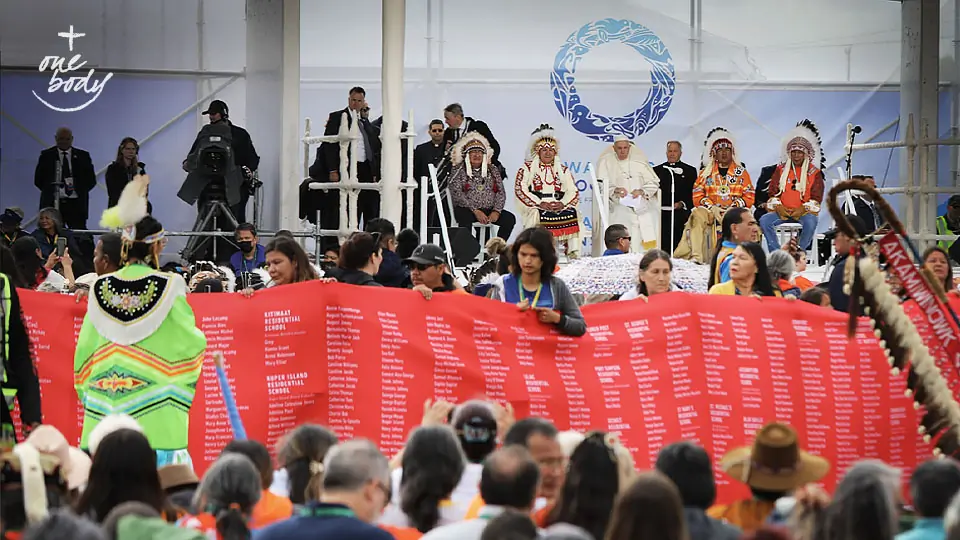 Maskwacis, Alberta: Pope Francis meets with Indigenous peoples, First Nations, Métis and Inuit on the former grounds of the Ermineskin Residential School. A green-clad dancer stands in front of a long red banner containing the names of victims of residential schools