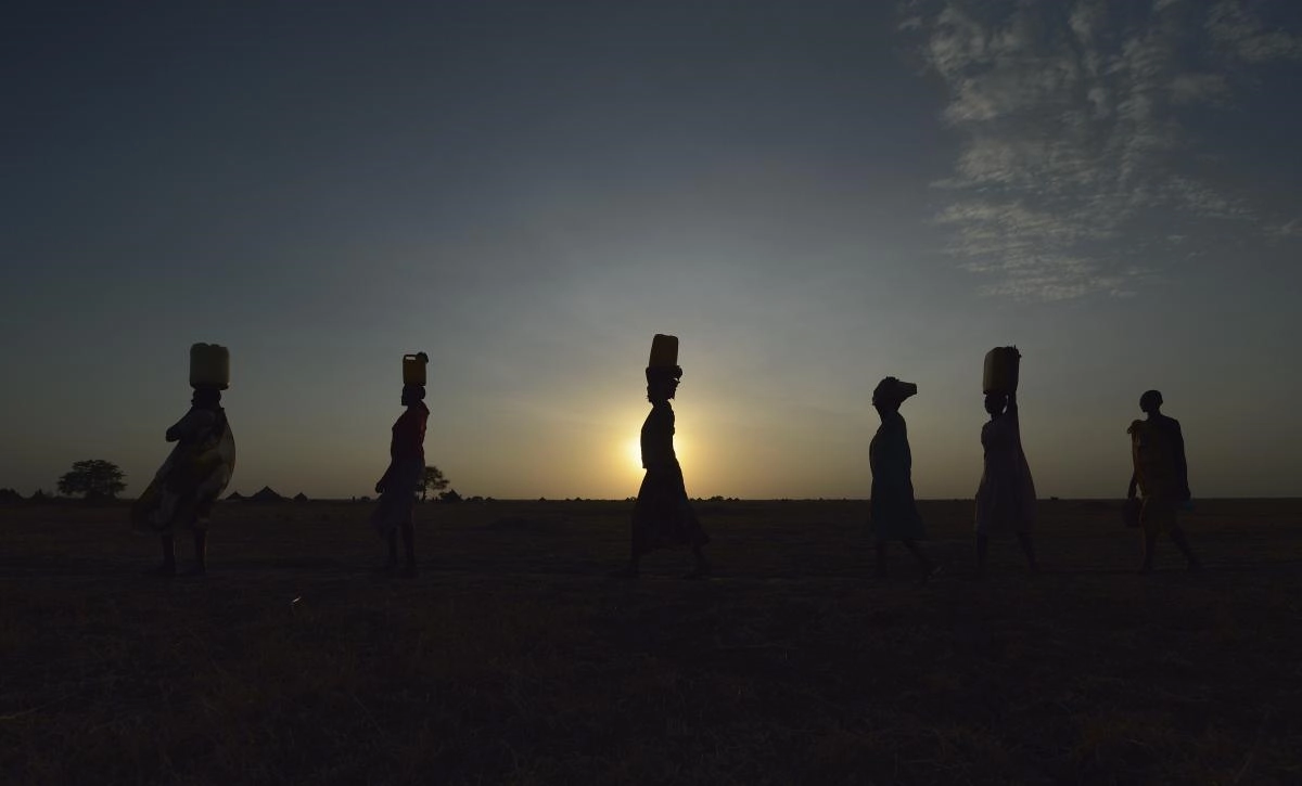   Women carry water to their homes at sunrise in Dong Boma, a Dinka village in South Sudan's Jonglei State. The women obtained water from a well drilled by the Lutheran World Federation, a member of the ACT Alliance, which is helping villagers restart their lives with support for housing, livelihood, and food security