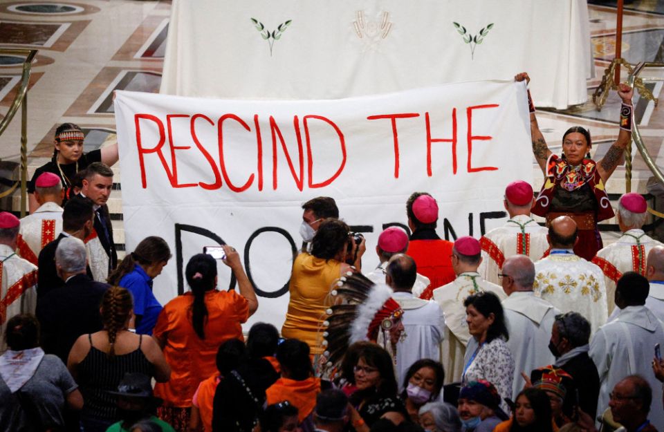 Indigenous people hold a banner calling on Pope Francis to 'rescind the doctrine,' an apparent reference to the so-called Doctrine of Discovery, a collection of old papal teachings that encouraged explorers to colonize and claim the lands of any people who were not Christian, placing both the land and the people under the sovereignty of European Christian rulers. The incident occurred during a papal Mass at the National Shrine of Sainte-Anne-de-Beaupré in Quebec